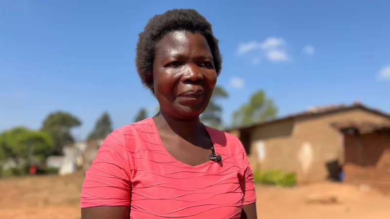 Dorothy Masasa(in a pink blouse )standing on a compound with a house in the background.