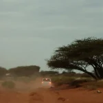 In the distance; the brake lights of a white saloon car traveling on a dusty desert road.