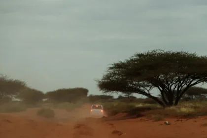 In the distance; the brake lights of a white saloon car traveling on a dusty desert road.