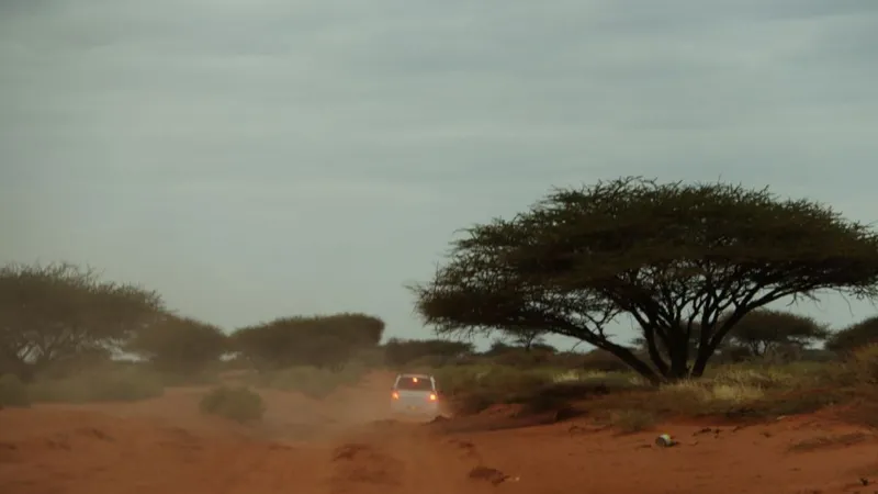 In the distance; the brake lights of a white saloon car traveling on a dusty desert road.