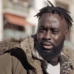 A close-up picture of Menka Gomis with short dreadlocks and a brown winter jacket