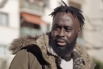 A close-up picture of Menka Gomis with short dreadlocks and a brown winter jacket